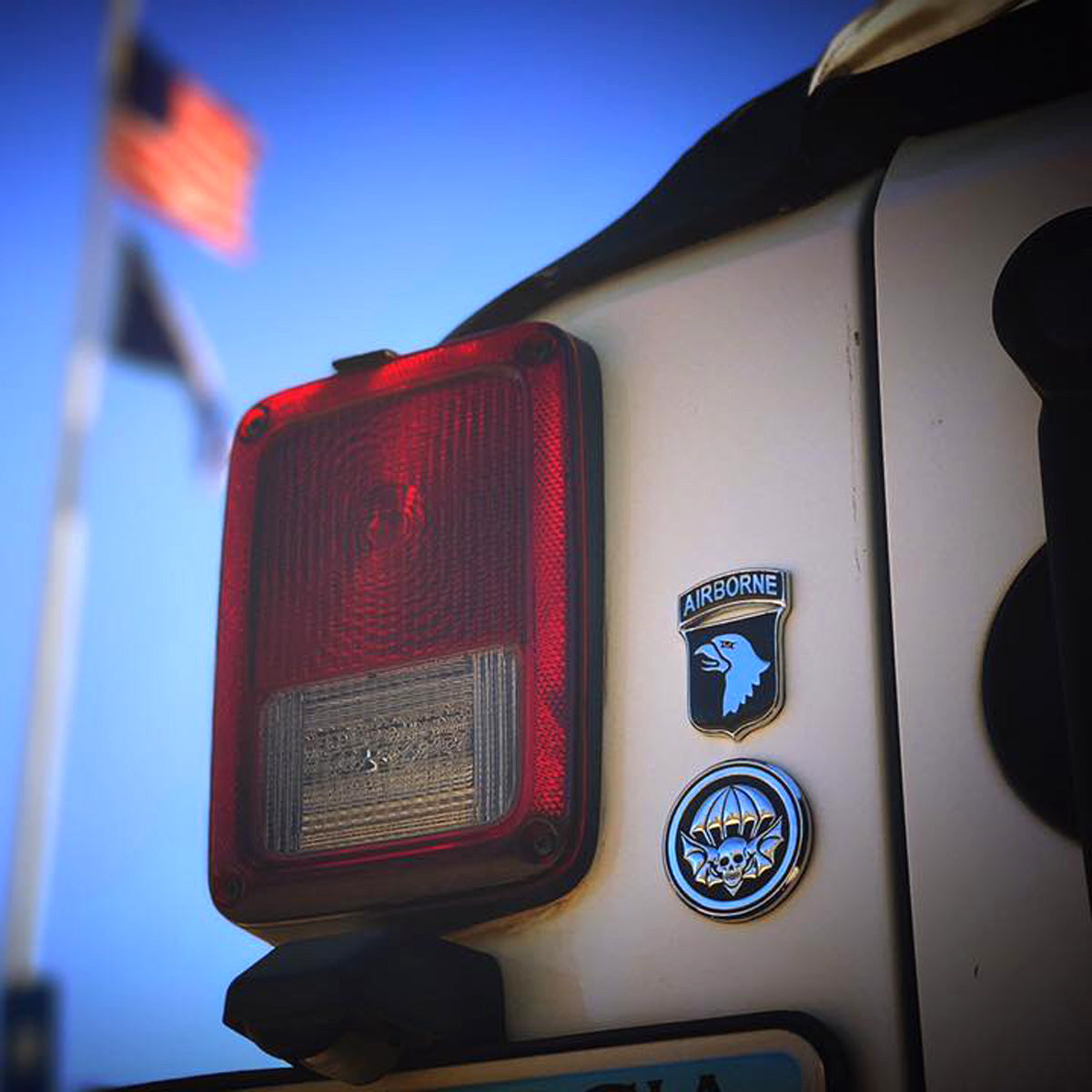 A close-up of a vehicle tail light with a chrome-plated, zinc alloy badge featuring a black enamel round winged-skull patch, attached by 3M adhesive.